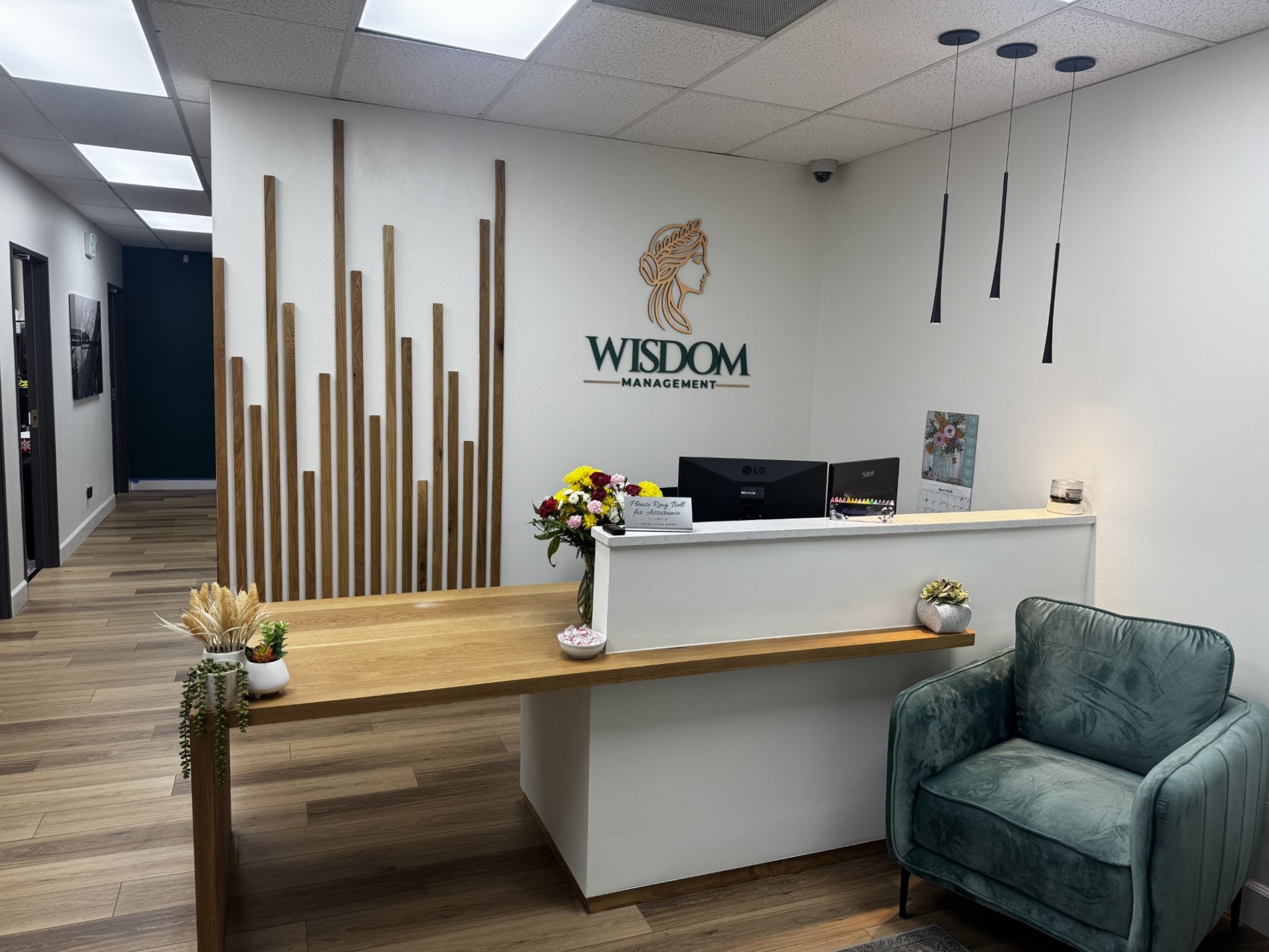 Reception area of the newly remodeled Wisdom Management office, featuring the company logo behind the front desk, modern wood accents, and seating prepared for the open house.